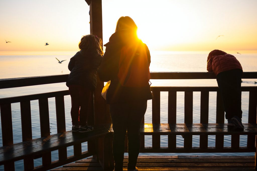 Mother with her two children at the seaside watching a sunset over the ocean